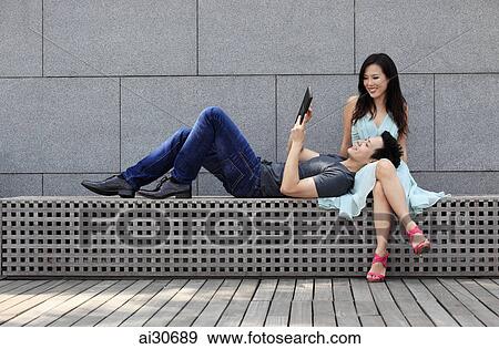 Stock Photo - Young couple sitting together looking at digital tablet. Fotosearch