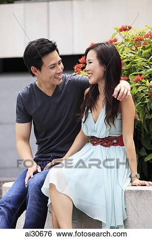 Young couple smiling and sitting together outdoors. View Large Photo Image Stock Photograph - Young couple smiling and sitting together outdoors.. Fotosearch