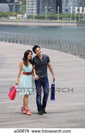Young couple walking together holding hands and shopping bags View Large Photo Image Stock Photo - Young couple walking together holding hands and shopping bags. Fotosearch