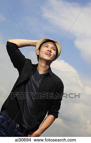 Young man holding his hat smiling View Large Photo Image Picture - Young man holding his hat smiling. Fotosearch