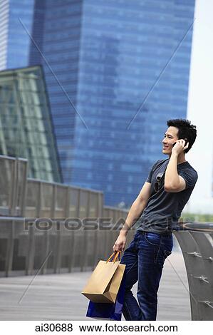 Young man holding shopping bags and talking on phone View Large Photo Image Stock Photo - Young man holding shopping bags and talking on phone. Fotosearch