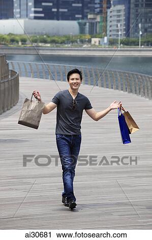 Stock Image - Young man holding shopping bags in the air smiling. Fotosearch