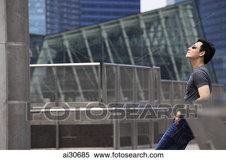 Young man leaning against railing wearing sunglasses looking up View Large Photo Image Stock Photography - Young man leaning against railing wearing sunglasses looking up. Fotosearch
