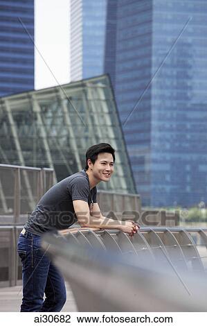 Stock Image - Young man leaning on railing looking at view and smiling. Fotosearch