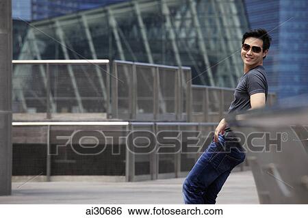 Young man leaning on railing wearing sunglasses and smiling. View Large Photo Image Stock Photograph - Young man leaning on railing wearing sunglasses and smiling.. Fotosearch