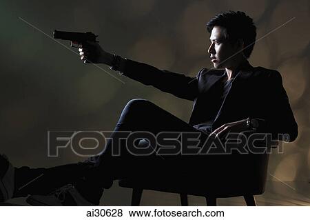 Young man sitting down pointing a gun View Large Photo Image Stock Photo - Young man sitting down pointing a gun. Fotosearch