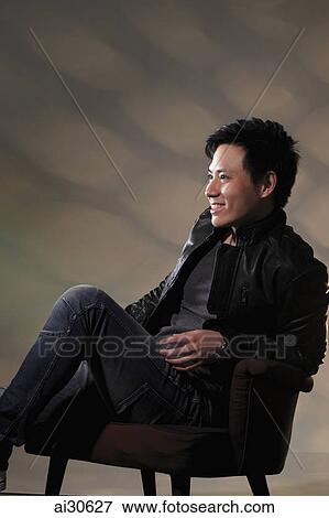 Stock Photo - Young man sitting in chair smiling.. Fotosearch