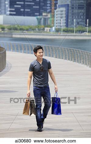 Young man walking on boardwalk holding shopping bags View Large Photo Image Stock Image - Young man walking on boardwalk holding shopping bags. Fotosearch