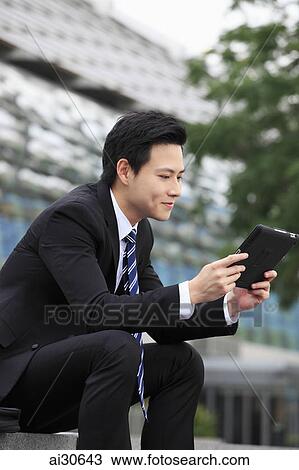 Stock Image - Young man wearing a business suit holding digital tablet.. Fotosearch