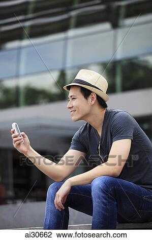 Young man wearing a hat looking at phone and smiling. View Large Photo Image Stock Image - Young man wearing a hat looking at phone and smiling.. Fotosearch