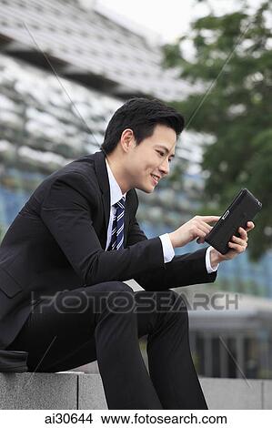 Picture - Young man wearing a suit looking at a digital tablet. Fotosearch