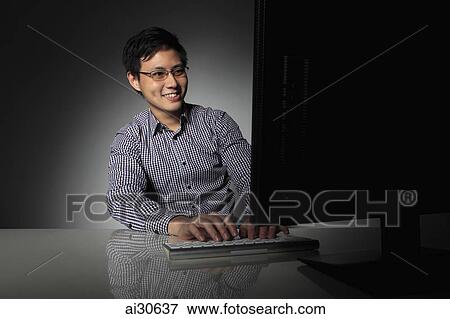 Stock Photo - Young man working on computer smiling. Fotosearch