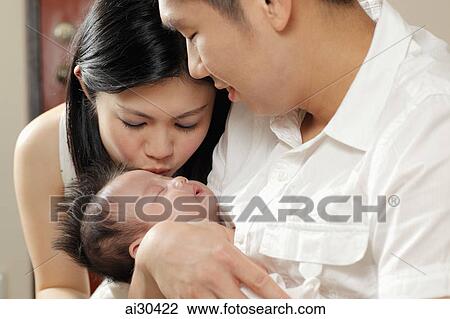 Stock Image - Young mother kisses her sleeping baby while father looks on. Fotosearch