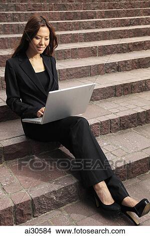 Young woman in a business suit, sitting on steps using a laptop View Large Photo Image Picture - Young woman in a business suit, sitting on steps using a laptop. Fotosearch