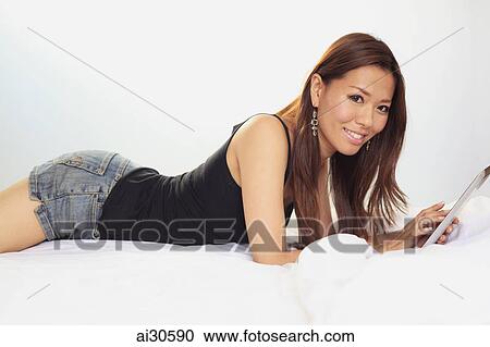 Young woman laying on bed using a digital tablet View Large Photo Image Stock Image - Young woman laying on bed using a digital tablet. Fotosearch