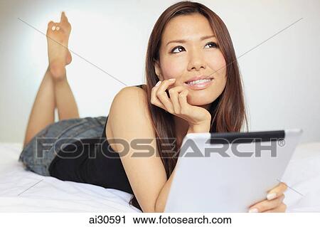 Young woman laying on her stomach using a digital tablet View Large Photo Image Stock Image - Young woman laying on her stomach using a digital tablet. Fotosearch