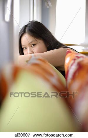 Young woman peering out from behind her arm, pillows in foreground View Large Photo Image Stock Photo - Young woman peering out from behind her arm, pillows in foreground. Fotosearch