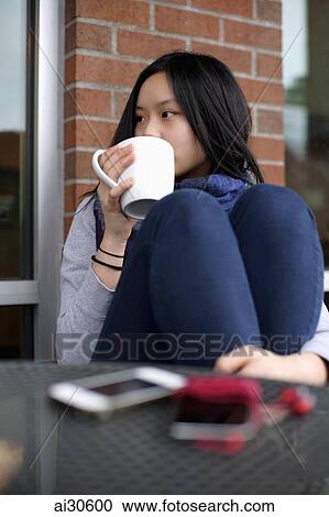 Young woman sitting at a cafe, drinking coffee View Large Photo Image Stock Image - Young woman sitting at a cafe, drinking coffee. Fotosearch