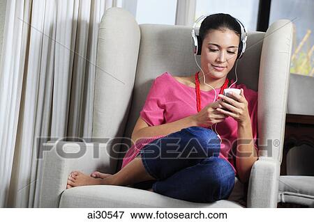 Young woman sitting in a comfy chair, listening to music View Large Photo Image Stock Photo - Young woman sitting in a comfy chair, listening to music. Fotosearch