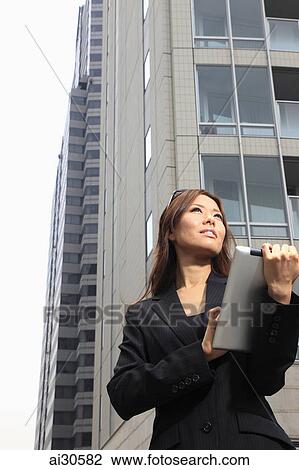 Stock Image - Young woman standing in front of a building holding a digital tablet. Fotosearch