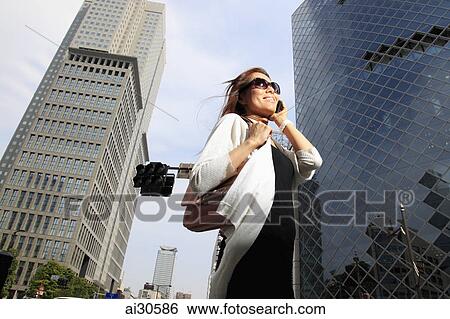 Young woman talking on the phone in front of buildings View Large Photo Image Stock Photograph - Young woman talking on the phone in front of buildings. Fotosearch