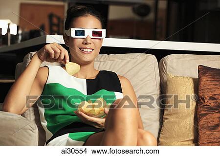 Young woman wearing 3D glasses and watching a movie while eating snacks View Large Photo Image Picture - Young woman wearing 3D glasses and watching a movie while eating snacks. Fotosearch
