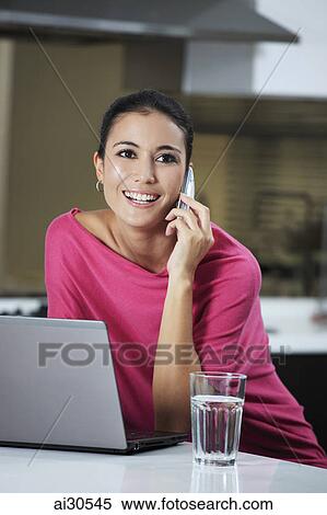 Young woman working on a laptop and talking on the phone View Large Photo Image Stock Photography - Young woman working on a laptop and talking on the phone. Fotosearch