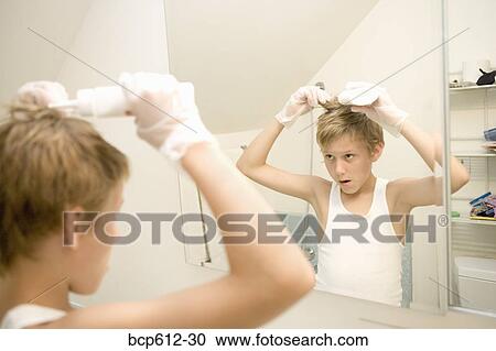 Stock Image - Boy dying hair in bathroom mirror. Fotosearch