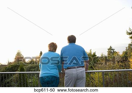 Couple standing at railing looking at view View Large Photo Image Stock Image - Couple standing at railing looking at view. Fotosearch