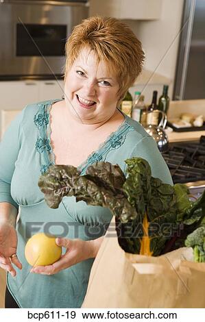 Stock Photo - Friendly woman with produce in kitchen. Fotosearch