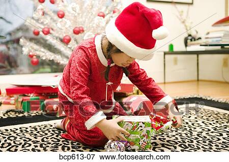 Girl in santa hat unwrapping present View Large Photo Image Stock Photo - Girl in santa hat unwrapping present. Fotosearch