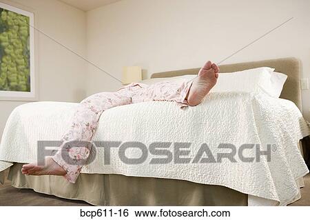 Stock Photograph - Legs of woman sprawled on bed in pajamas. Fotosearch