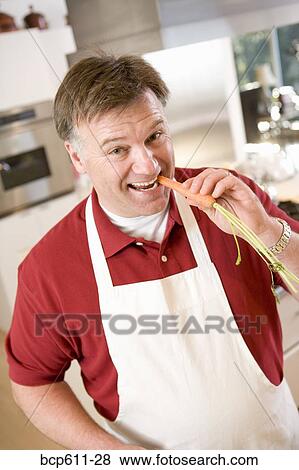 Man in apron biting into carrot View Large Photo Image Stock Photo - Man in apron biting into carrot. Fotosearch
