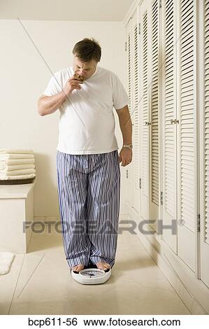 Stock Photograph - Overweight man eating cookie on scale. Fotosearch