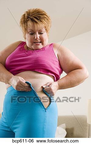 Stock Photograph - Overweight woman squeezing into tight pants. Fotosearch