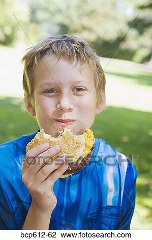 Stock Image - Portrait of boy eating hamburger outside. Fotosearch
