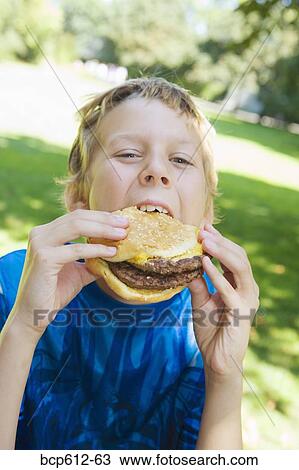 Stock Image - Portrait of boy eating hamburger outside. Fotosearch