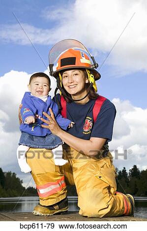 Stock Photo - Portrait of female firefighter holding baby. Fotosearch
