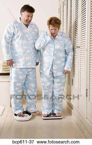 Shocked woman on bathroom scale with husband View Large Photo Image Stock Photo - Shocked woman on bathroom scale with husband. Fotosearch