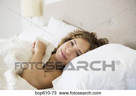 Stock Image - Smiling tired woman in bed. Fotosearch