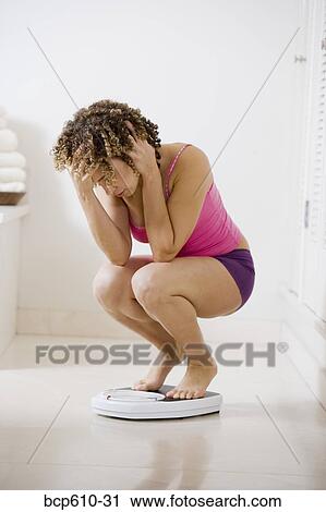 Stressed woman crouching on bathroom scale View Large Photo Image Stock Image - Stressed woman crouching on bathroom scale. Fotosearch