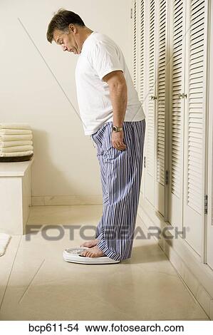 Picture - Surprised overweight man on bathroom scale. Fotosearch