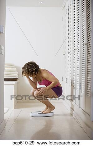 Upset woman crouching on bathroom scale View Large Photo Image Stock Photo - Upset woman crouching on bathroom scale. Fotosearch