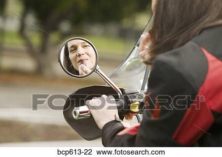 Woman applying lipstick in motorcycle mirror View Large Photo Image Stock Image - Woman applying lipstick in motorcycle mirror. Fotosearch