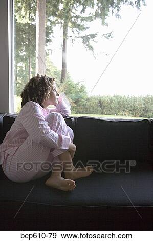 Stock Photo - Woman in pajamas looking out window. Fotosearch