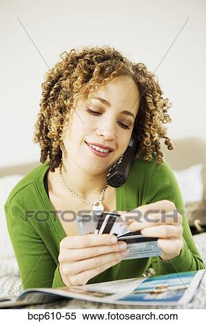 Stock Photography - Woman on phone choosing credit card. Fotosearch