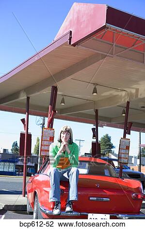 Stock Image - Woman sitting on sports car at drive-in. Fotosearch