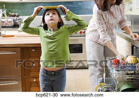 Stock Image - Daughter playing while mom unloads dishwasher. Fotosearch