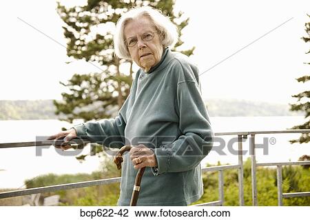 Stock Image - Elderly woman on balcony overlooking water. Fotosearch
