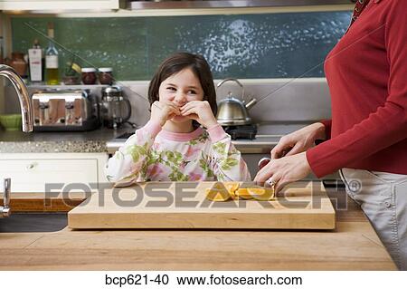 Stock Image - Girl eating orange slices while mom cuts them. Fotosearch